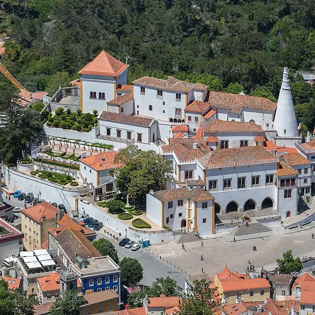 The Sintra National Palace seen from above, sitting among the roofs and gardens of Sintra's historic centre with one conical chimney visible.