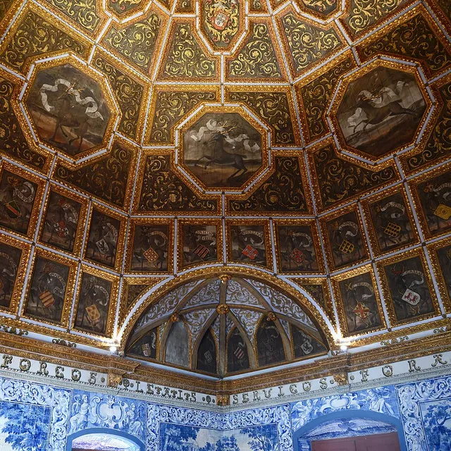 The gilded dome of the Sala dos Brasões in the Sintra National Palace, painted with stags, heraldic shields of 72 noble families and blue azulejo walls below.