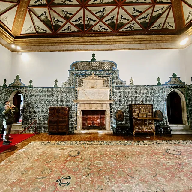 The Magpie Room of the Sintra National Palace: a beamed ceiling painted with magpies above green-and-white azulejo walls and a stone fireplace.